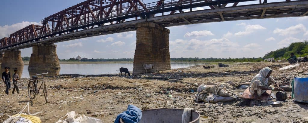 A poor woman from the dhobi, or clothes washing, caste, cleans pots along the waste-strewn banks of the Yamuna River at Dhobi Ghat, Agra; the famed Taj Mahal rises behind.